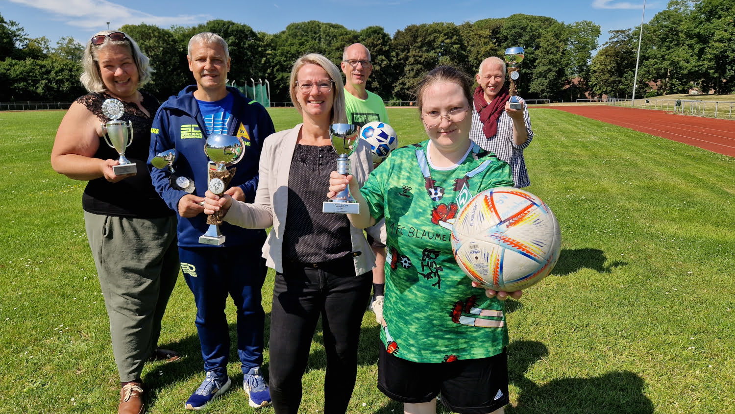 Beteiligte des inklusiven Fußballturniers mit Pokalen und Fußball im Stadion